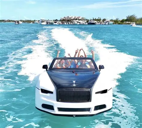 People cheer from a white car-shaped boat speeding through bright turquoise tropical water.