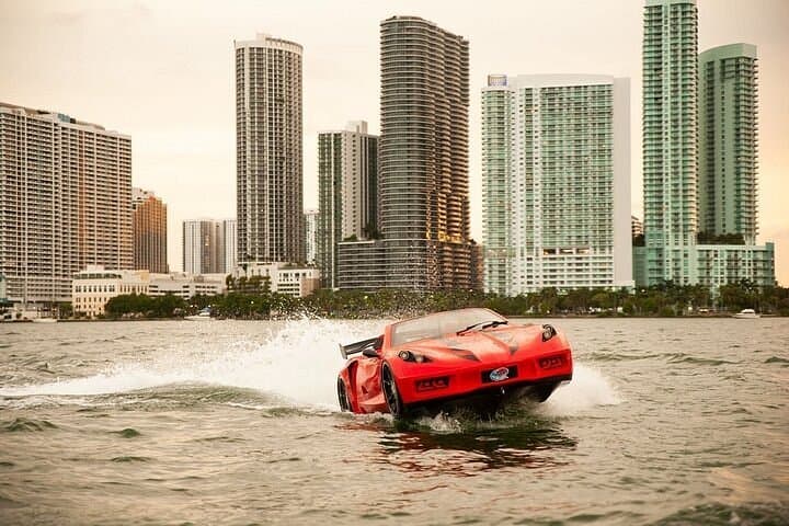 Red sports car-shaped boat speeding across the water with a modern city skyline background.